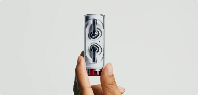 A hand holding a cylindrical, transparent charging case for Nothing Ear (stick) earbuds vertically.